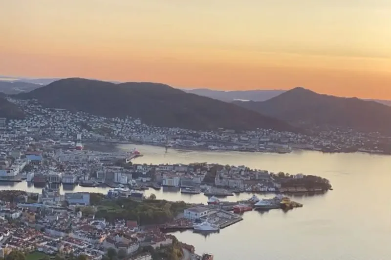 Bergen harbour from above at sunset, warm light on the water and the wharf, the city fading into the hills.