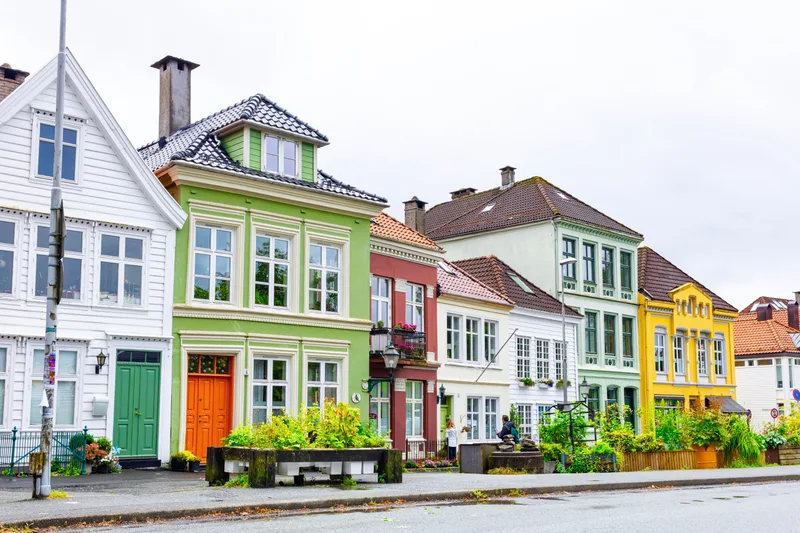 A row of painted wooden houses on a Bergen street, white, green, red and yellow facades under an overcast sky.