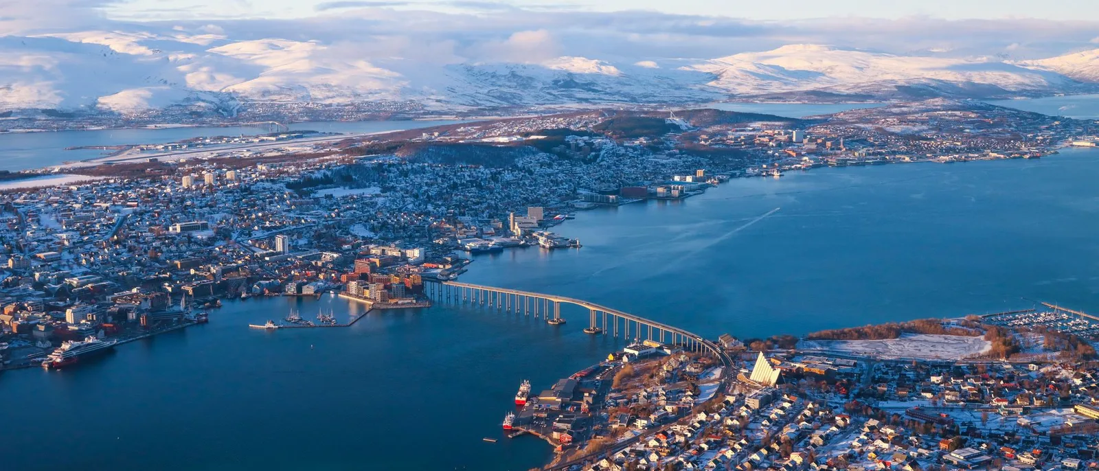 Tromsø from the mountain above it in winter, the bridge and the Arctic Cathedral, the sound and the snow-covered ranges beyond.