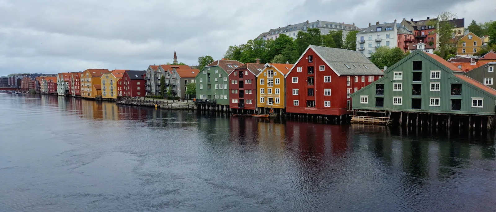 Die bunten Speicherhäuser am Fluss in Trondheim, auf Pfählen über dem Wasser, dahinter die Stadt am Hang.