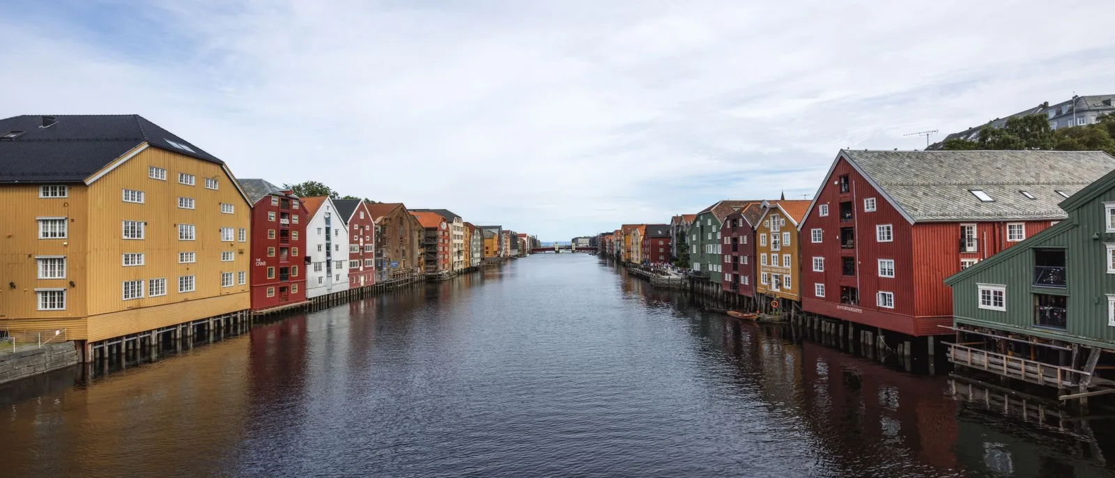 The Nidelva in Trondheim seen straight down the channel, the old timber wharf buildings lining both banks under a wide sky.