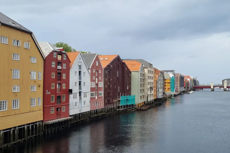Painted timber wharf houses on stilts along the Nidelva river in Trondheim under a grey sky.